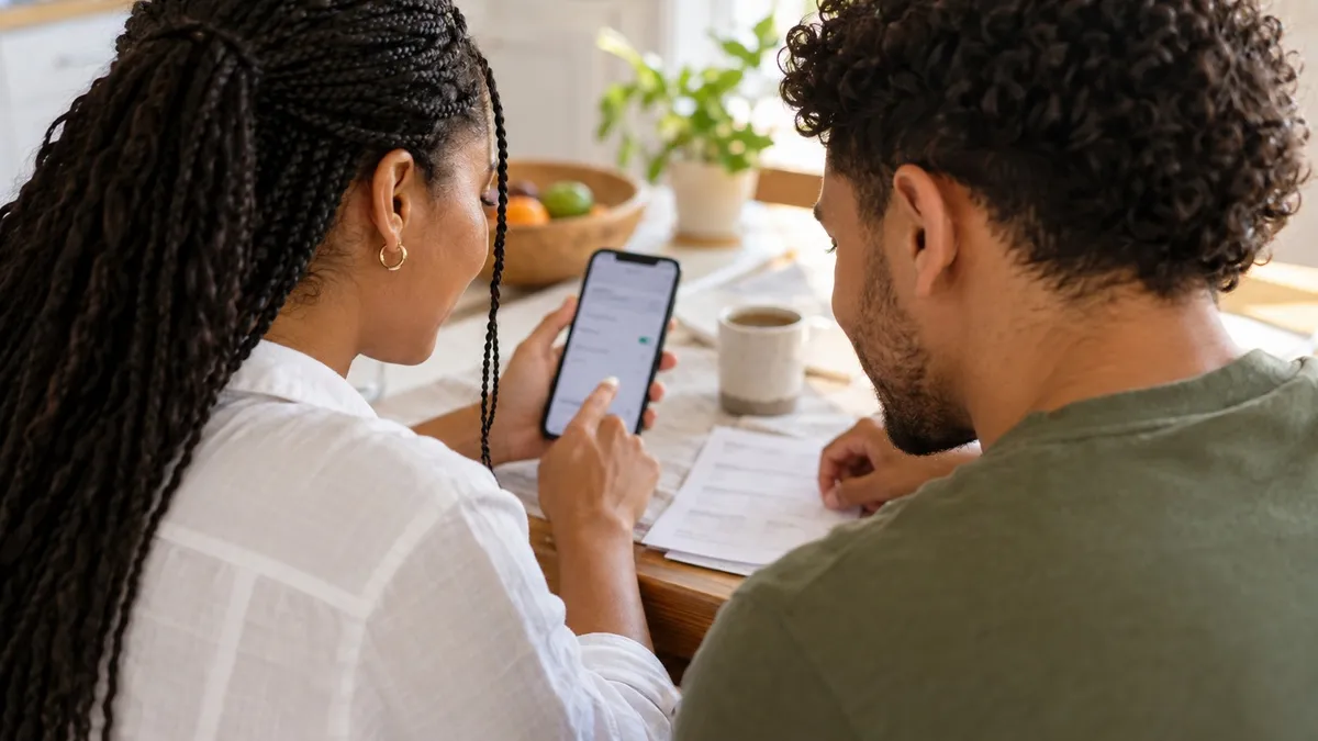 Couple setting up a monthly transfer on a phone at their kitchen table.